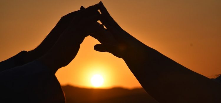 the sun is setting behind two hands making a heart shape